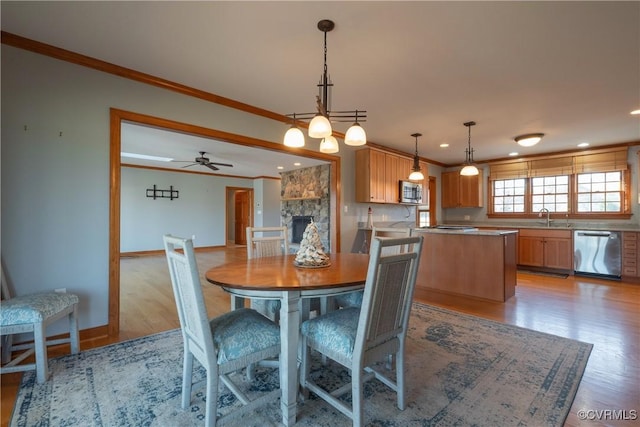 dining room with a stone fireplace, crown molding, sink, light hardwood / wood-style flooring, and ceiling fan