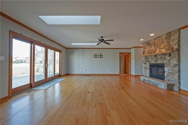 unfurnished living room with a skylight, a fireplace, ornamental molding, and light hardwood / wood-style flooring