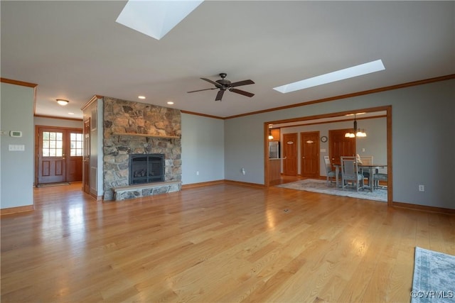 unfurnished living room with a skylight, crown molding, light hardwood / wood-style floors, a fireplace, and ceiling fan with notable chandelier