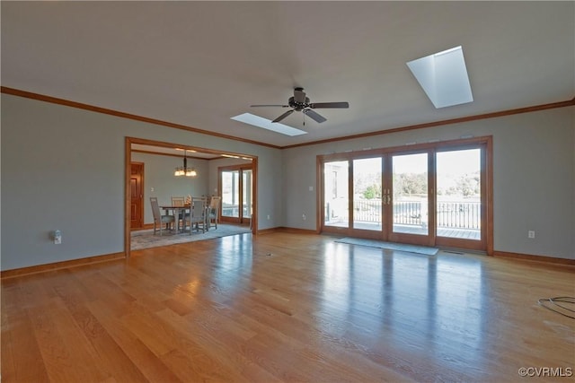 unfurnished living room with ceiling fan with notable chandelier, a skylight, ornamental molding, and light hardwood / wood-style flooring