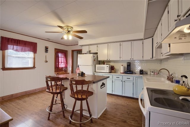 kitchen featuring white appliances, sink, hardwood / wood-style flooring, tasteful backsplash, and white cabinetry