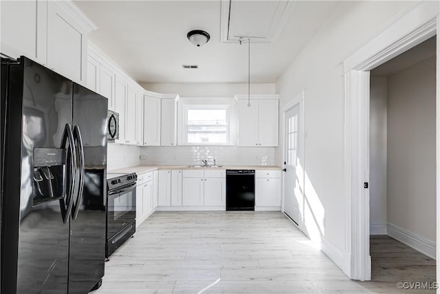 kitchen featuring sink, tasteful backsplash, white cabinets, black appliances, and light wood-type flooring