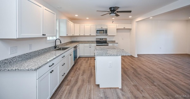 kitchen with light stone countertops, a center island, sink, stainless steel appliances, and white cabinets