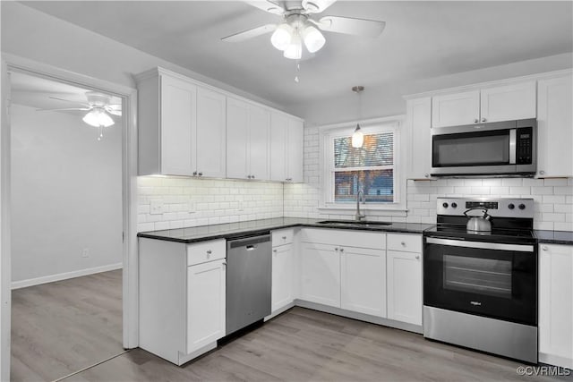 kitchen featuring pendant lighting, appliances with stainless steel finishes, white cabinetry, sink, and light hardwood / wood-style flooring