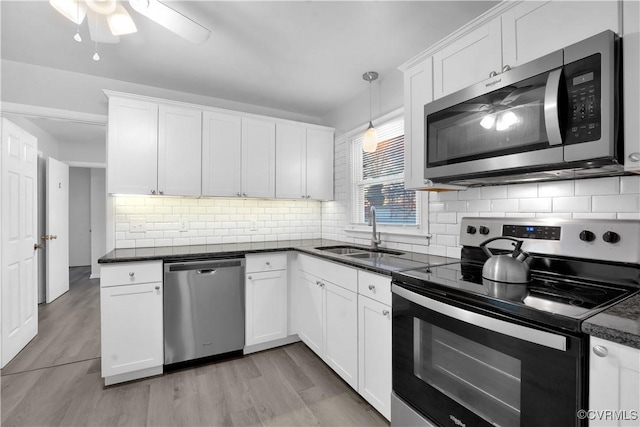 kitchen with pendant lighting, decorative backsplash, sink, white cabinetry, and stainless steel appliances