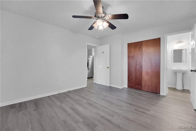 unfurnished bedroom featuring stainless steel refrigerator with ice dispenser, light hardwood / wood-style floors, a closet, ceiling fan, and ensuite bathroom