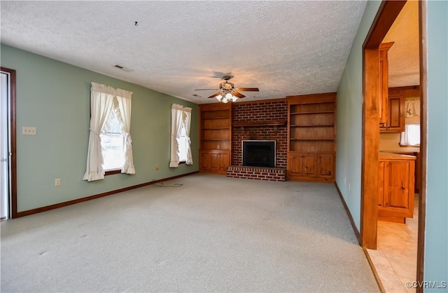 unfurnished living room with ceiling fan, a brick fireplace, built in features, light colored carpet, and a textured ceiling