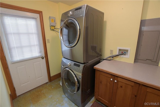 washroom with electric panel, stacked washer and dryer, and cabinets