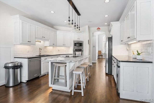 kitchen featuring a center island, sink, stainless steel appliances, decorative light fixtures, and white cabinets