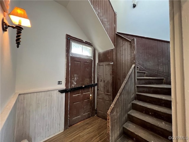 staircase featuring hardwood / wood-style flooring, wood walls, and vaulted ceiling