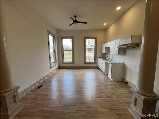 interior space with ceiling fan, sink, decorative columns, hardwood / wood-style floors, and white cabinets