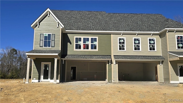 multi unit property with dirt driveway, a shingled roof, and an attached garage