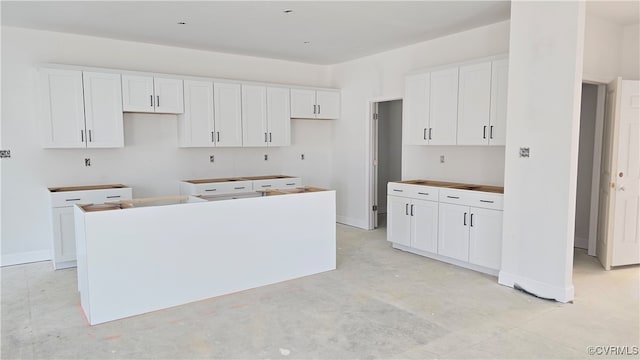 kitchen with baseboards, concrete floors, white cabinetry, and a center island