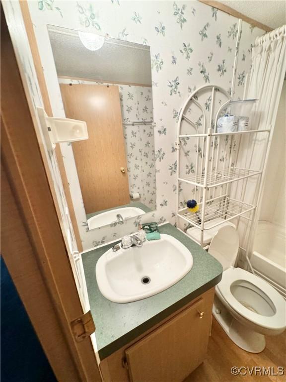 full bathroom featuring shower / bath combination with curtain, vanity, a textured ceiling, wood-type flooring, and toilet