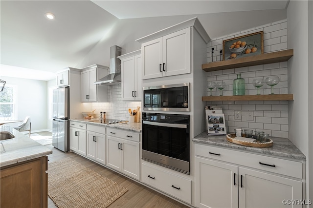 kitchen with white cabinets, wall chimney exhaust hood, lofted ceiling, and appliances with stainless steel finishes