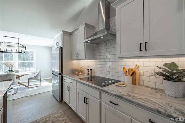 kitchen featuring black electric stovetop, backsplash, white cabinetry, and wall chimney range hood