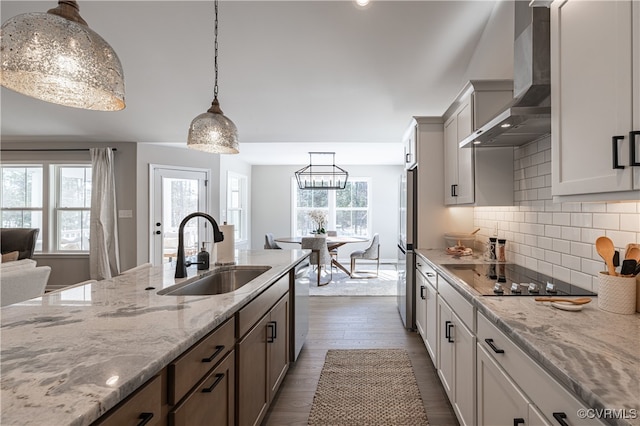 kitchen with wall chimney range hood, hanging light fixtures, sink, appliances with stainless steel finishes, and white cabinetry