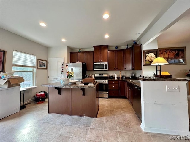 kitchen with dark brown cabinetry, stainless steel appliances, dark stone countertops, a breakfast bar area, and a kitchen island