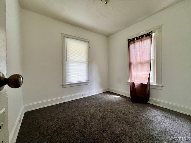 empty room featuring a wealth of natural light and dark carpet