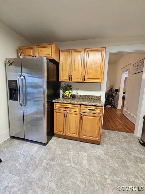 kitchen featuring stainless steel refrigerator with ice dispenser and dark stone counters