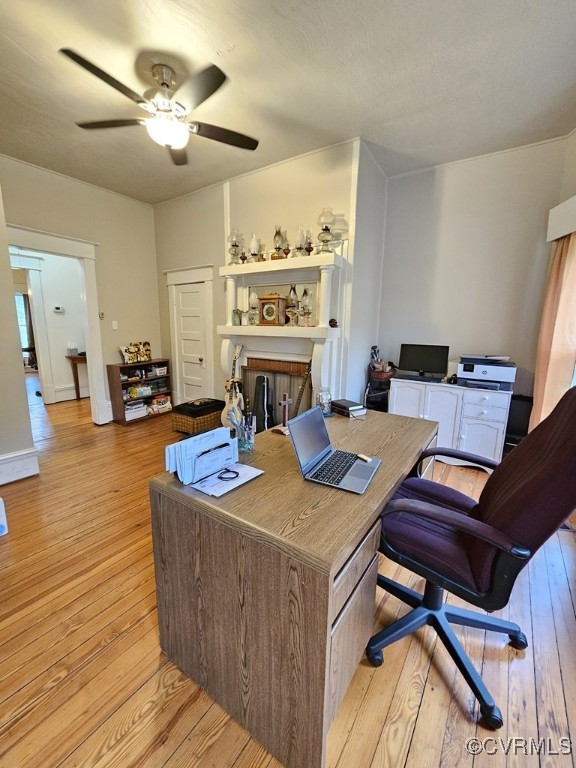 office area featuring a fireplace, a ceiling fan, and light wood-style flooring
