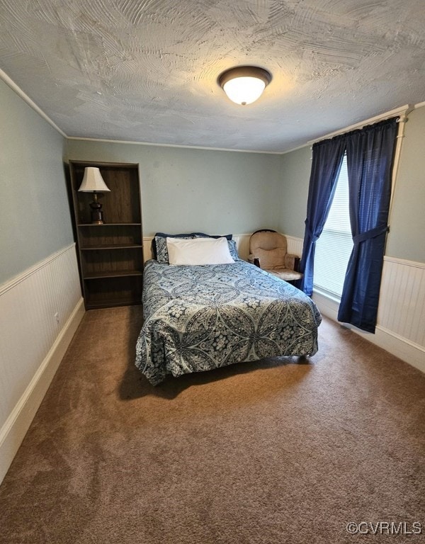 carpeted bedroom featuring a wainscoted wall and a textured ceiling