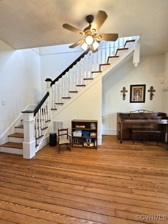 staircase featuring wood finished floors, visible vents, a ceiling fan, and baseboards