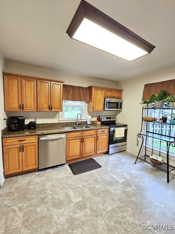 kitchen featuring stainless steel appliances, a sink, brown cabinets, and dark stone counters