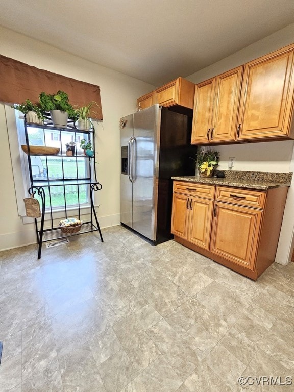 kitchen with stainless steel refrigerator with ice dispenser, stone countertops, visible vents, and baseboards