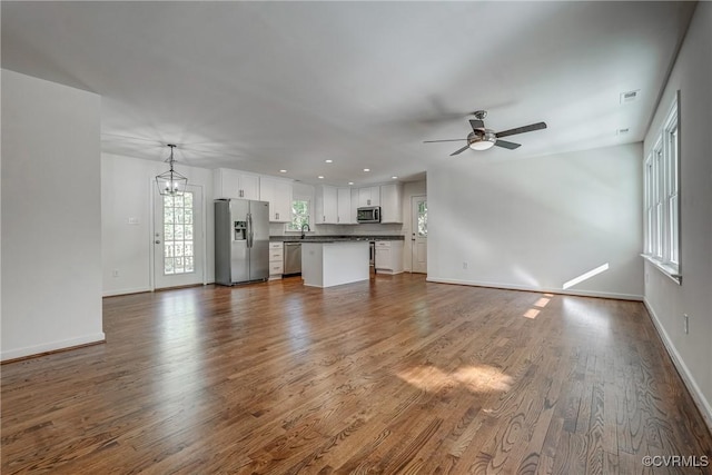 unfurnished living room featuring hardwood / wood-style flooring, ceiling fan with notable chandelier, and sink