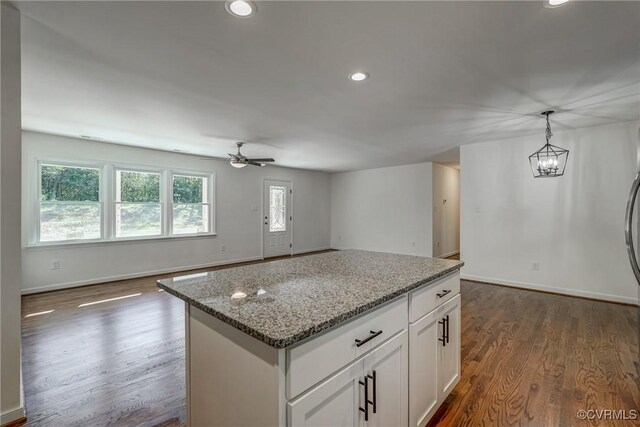 kitchen featuring ceiling fan, a center island, hanging light fixtures, light stone counters, and white cabinets