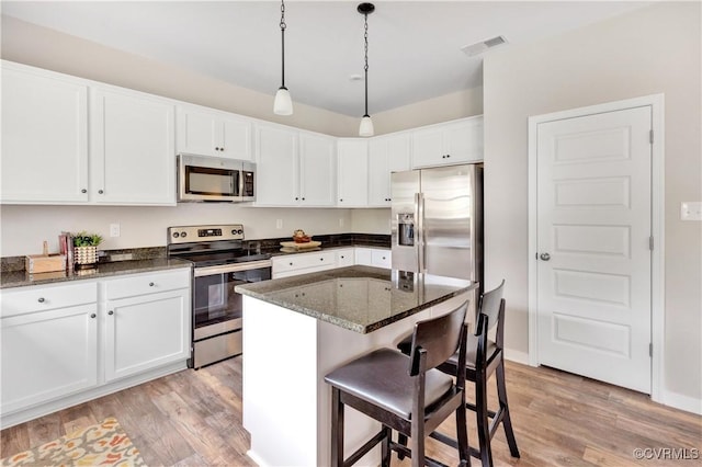 kitchen with appliances with stainless steel finishes, light wood-type flooring, dark stone counters, white cabinets, and a kitchen island