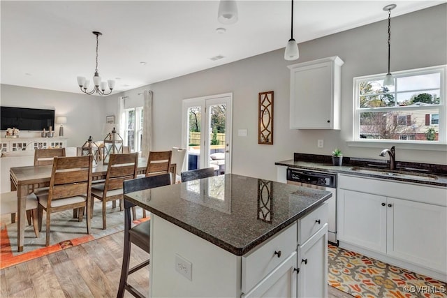 kitchen with sink, a kitchen island, dark stone countertops, dishwashing machine, and white cabinets