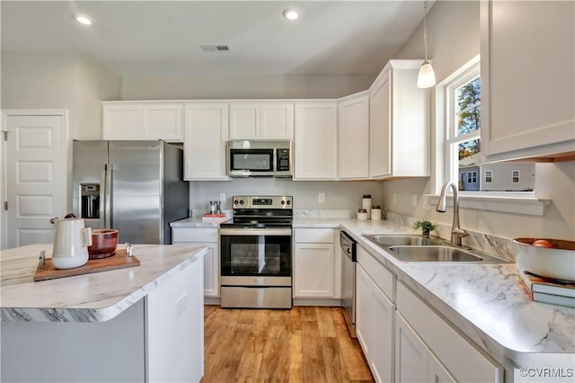 kitchen with white cabinetry, sink, stainless steel appliances, pendant lighting, and light wood-type flooring