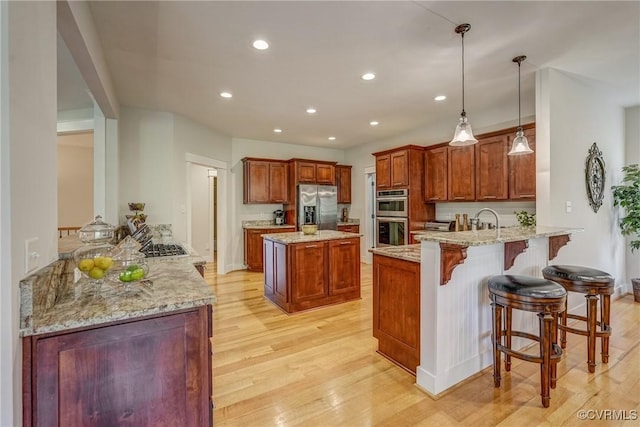 kitchen featuring kitchen peninsula, light hardwood / wood-style floors, pendant lighting, a kitchen bar, and appliances with stainless steel finishes