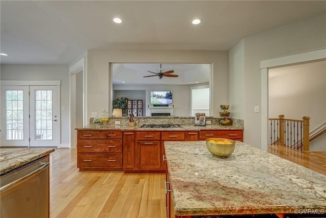 kitchen with ceiling fan, a center island, light stone counters, light hardwood / wood-style floors, and appliances with stainless steel finishes