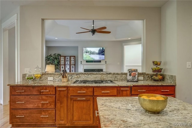 kitchen featuring ceiling fan, light stone counters, stainless steel gas cooktop, and a tray ceiling