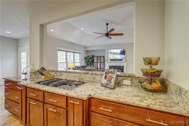 kitchen with stainless steel gas stovetop, light hardwood / wood-style floors, light stone countertops, and ceiling fan