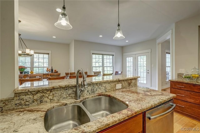 kitchen featuring sink, hanging light fixtures, stainless steel dishwasher, a wealth of natural light, and light stone counters