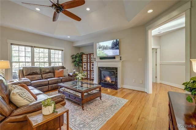 living room with a raised ceiling, ceiling fan, and light hardwood / wood-style floors