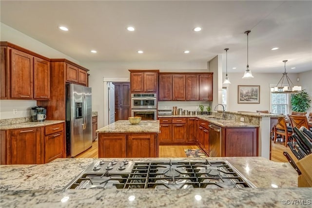 kitchen featuring kitchen peninsula, light stone countertops, stainless steel appliances, and decorative light fixtures