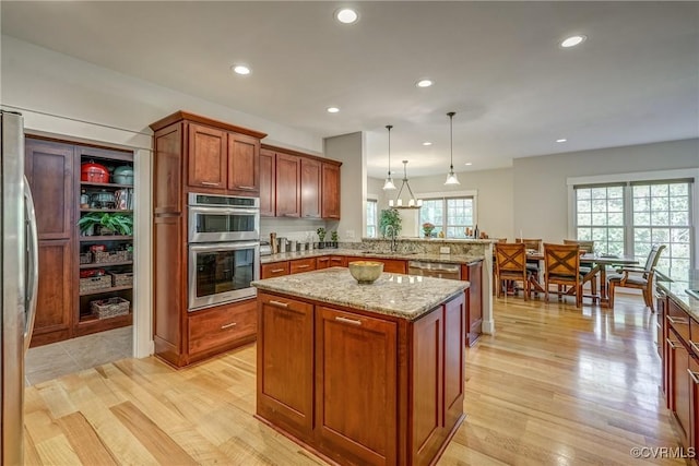 kitchen featuring light hardwood / wood-style flooring, light stone countertops, appliances with stainless steel finishes, decorative light fixtures, and a kitchen island