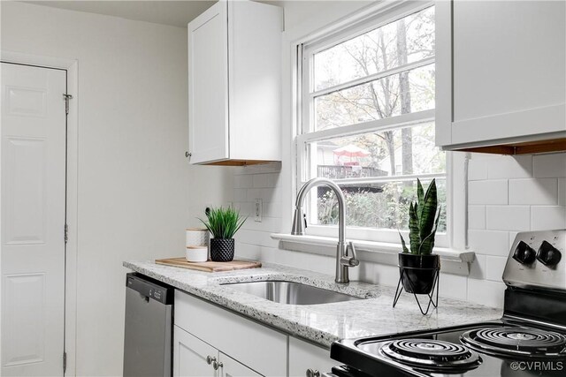 kitchen featuring white cabinets, decorative backsplash, stainless steel dishwasher, and light stone counters