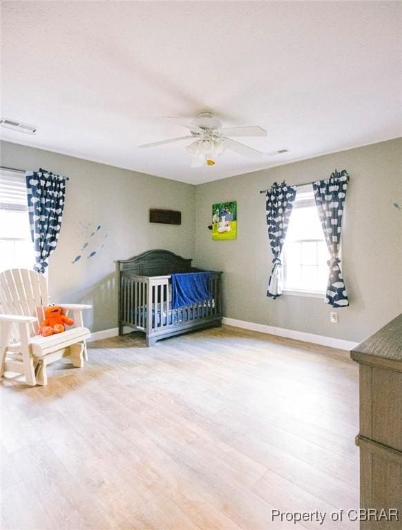 unfurnished bedroom featuring a crib, wood-type flooring, and ceiling fan