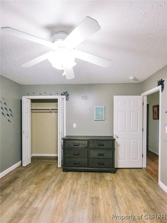 unfurnished bedroom with a textured ceiling, light wood-type flooring, a closet, and ceiling fan