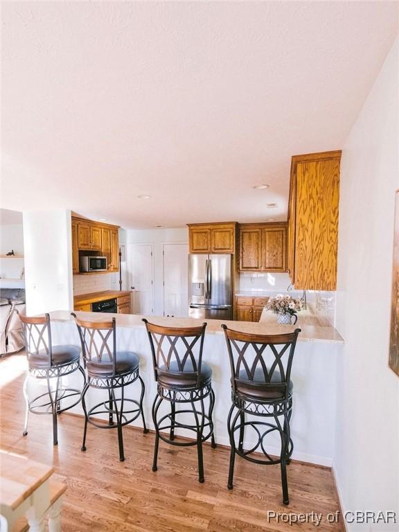 kitchen with a breakfast bar area, kitchen peninsula, stainless steel appliances, and light hardwood / wood-style floors