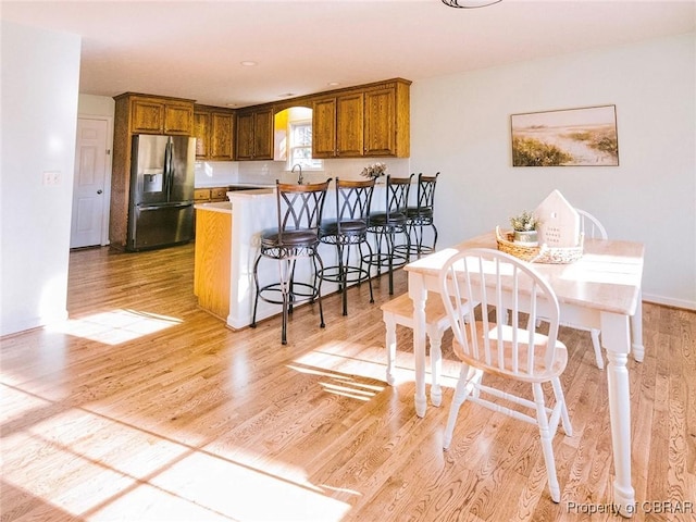 kitchen with kitchen peninsula, a breakfast bar, sink, stainless steel fridge with ice dispenser, and light hardwood / wood-style floors