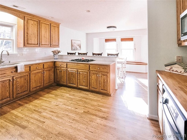 kitchen with kitchen peninsula, backsplash, light hardwood / wood-style floors, and sink