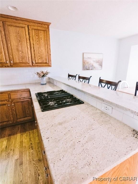 kitchen featuring dark hardwood / wood-style flooring, black gas cooktop, light stone counters, and a breakfast bar area