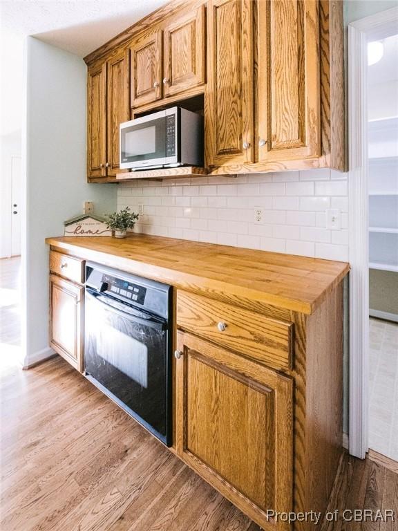 kitchen featuring light wood-type flooring, butcher block countertops, oven, and backsplash